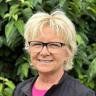 Orthodontic Assistant and Clinic Coordinator Kelly Smiling In Front Of A Hedge